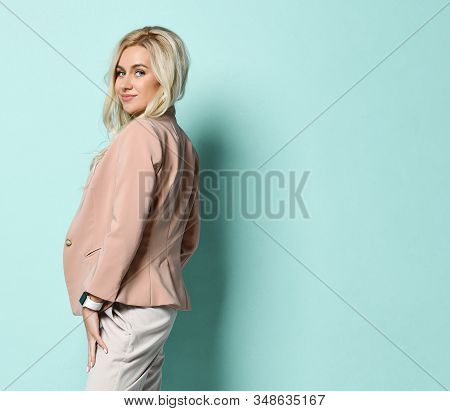 Blonde Woman In Beige Jacket And White Overall. There Is Watch On Her Hand. Smiling, Touching Her Ha