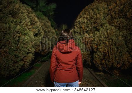 A Woman At Night In The Park Is A View From Behind. Theres A Dark Alley Ahead