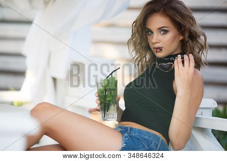 Beautiful Young Woman Enjoy Enjoys A Smoothie And Relax On Tropical Beach With Palm Tree. Summer Vac