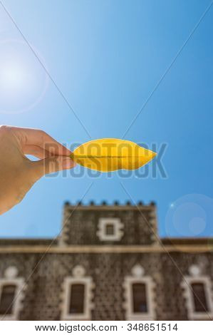 Female Hand Holding Yellow Leaf On The Church Of The Primacy Of Saint Peter Background. Tabgha, Isra