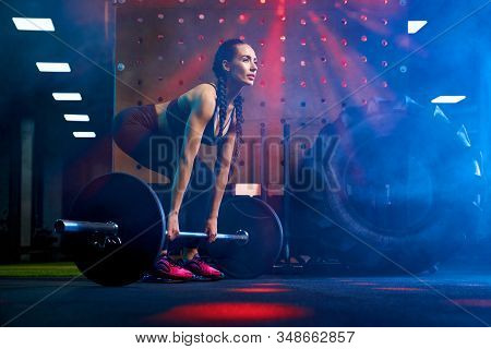 Side View Of Brunette Female Bodybuilder With Long Braids Doing Deadlift Using Barbell. Srtong Woman
