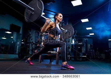 Side View Of Brunette Female Bodybuilder With Long Braids Doing Squats Using Barbell. Srtong Woman W