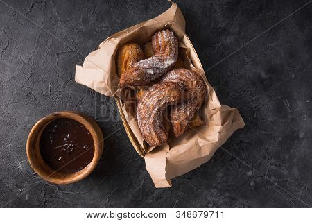 Churros With Sugar And Chocolate Sauce On Black Background. Top View. Churro Sticks In A Paper Bag. 