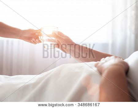 Social Worker Gives An Elderly Woman A Disabled Person A Mug Of Water On A Background Of A Window Wi