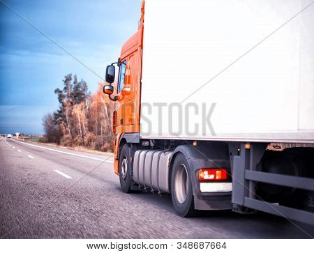 An Orange Truck Is Transporting Goods In A Refrigerated Trailer On A Motorway. Logistics And Industr