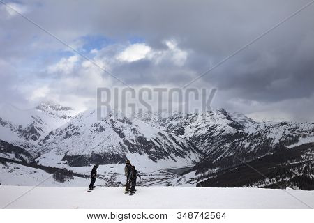 Group Of Snowboarders Starts On Off-piste Descent. High Snowy Mountains And Cloudy Storm Sky At Wint