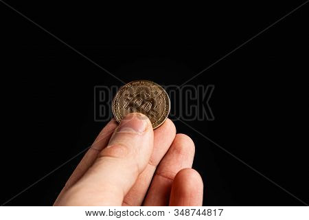 Bitcoin Coin In A Hand On A Black Background. Stock Photo Man Holding A Coin.