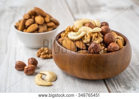 Different Nuts In White And Wooden Bowls On Wood Table