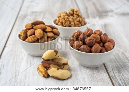 Different Nuts In White Bowls On Wood Table