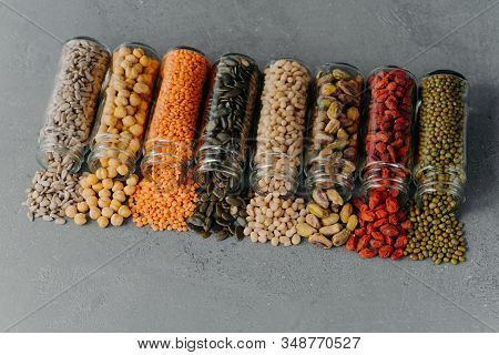 Nutitious Grains Spilled From Glass Bottles On Grey Texture Background. Jars With Different Kinds Of