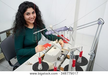 Young Dressmaker Using Professional Overlock Sewing Machine In Workshop Studio. Equipment For Edging