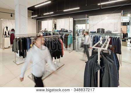 Blurred motion of sales consultants in clothing store with racks and accessories on shelves