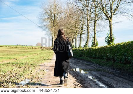 Attractive Girl In Long Black Winter Coat Walking Though The Muddy Paths Of The Flemish Countryside,