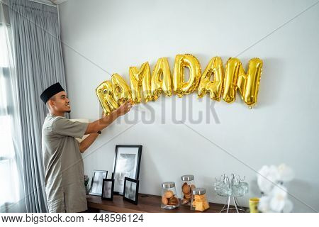 Muslim Male Decorating The Wall With Ramadan Balloon Text