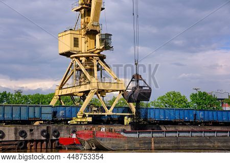 River Port Crane With Clamshell Or Griper Loading Coal To River Drag Boats Or Barges Moored By Pier 