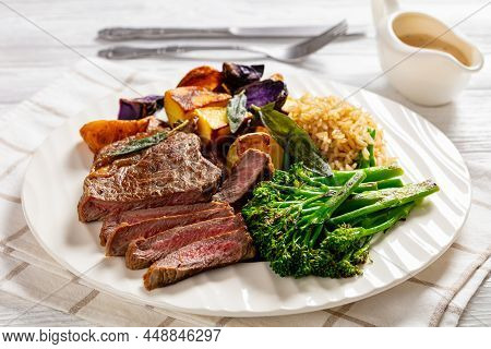 Steak With Mustard Sauce, Broccolini, Rice And Baked Rainbow Potatoes On A White Wooden Background, 