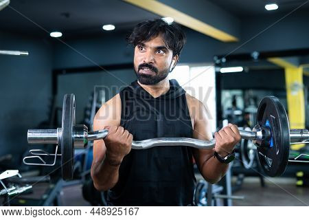 Young Indian Bodybuilder Busy Doing Biceps Workout By Lifting Weight Using Barbells At Gym - Concept