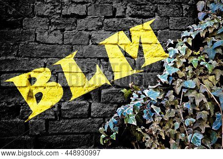 Blm Yellow Graffiti On Black Brick Wall With Ivy Plant, Symbol Of Social Movement Black Lives Matter