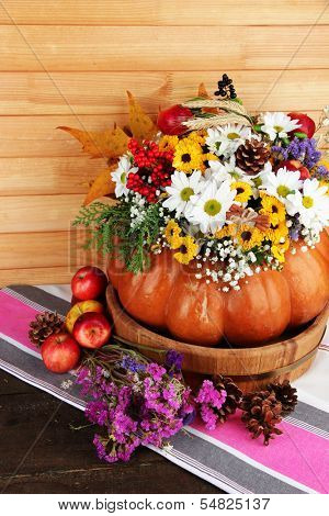 Beautiful autumn composition in pumpkin with apples and bumps on table on wooden background