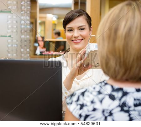Young female optometrist measuring pupilary distance on senior customer