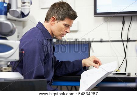 Engineer Looking At Plans With CMM Arm In Foreground