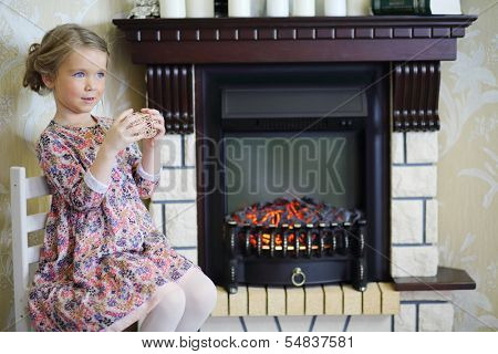 Little cute girl with straw balls sits on chair near fireplace in cosy room and looks away. 