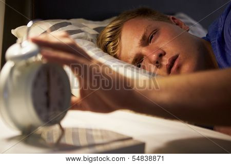 Teenage Boy Waking Up In Bed And Turning Off Alarm Clock