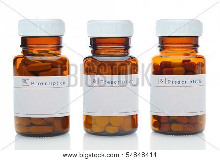 Closeup of three brown medicine bottles filled with different pills and medications with their caps on over a white background with reflection. 