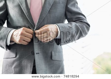 Midsection of mature businessman buttoning his blazer