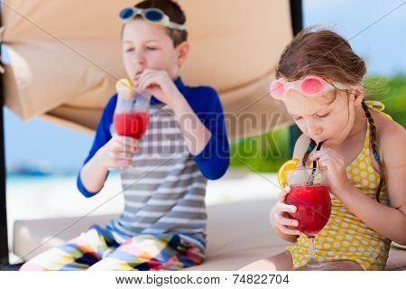 Kids at luxury resort relaxing at beach cabana and drinking tropical juices