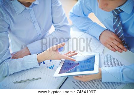 Two employees discussing business document in touchpad at meeting