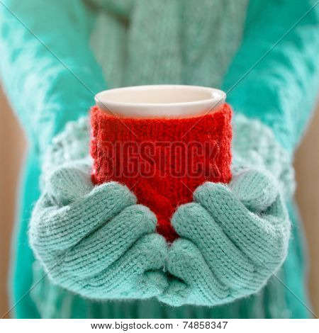 Woman holding winter cup close up on light background. Woman hands in teal gloves holding a cozy mug with hot cocoa, tea or coffee and a candy cane. Winter and Christmas time concept. 