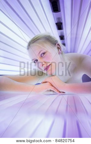 Pretty, young woman tanning her skin in a modern solarium/sunbed. Getting an energy boost during dark winter days.