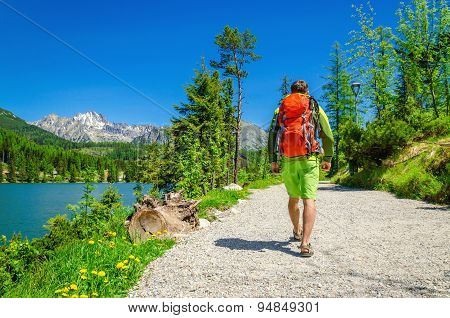 Man with backpack walks mountain trail by lake
