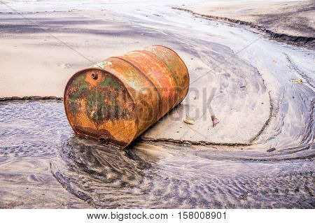 Rusty barrel oil on a partly black coloured beach illustrates the pollution of environment by oil spills