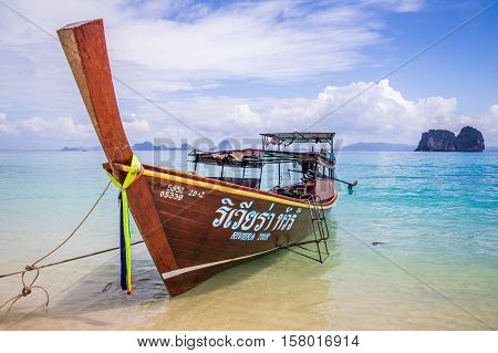 Longtail boat in crystal clear blue waters waiting for passengers on beautiful white beach in Ko Mok, Thailand