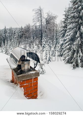 Renovated brick chimney with stainless steel cover covered with snow in winter time. Residential house chimney maintenance theme.
