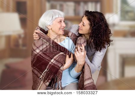 elderly woman and her daughter sitting in a chair with a blanket hug. mother. grandmother