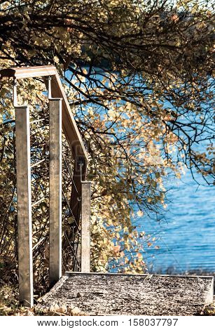 autumn nature, lake landscape with a small staircase leading to the water in the foreground trees, sunny evening, ribbed by waves of pond water, processed,
