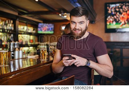 Happy handsome young man sitting and using mobile phone in pub