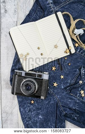 Old photo camera and notebook on the wooden background. Accessories: branches, heather and jeans cloth