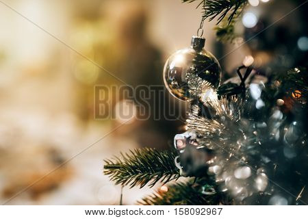 Closeup of decorations hanging from the branches of a Christmas tree in a home with people in the background