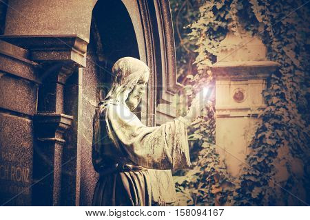Statue of a Jesus Christ with light effect. Olsany Cemetery, the largest graveyard in Prague, Czech Republic. Summer time with moody, dark sepia colors