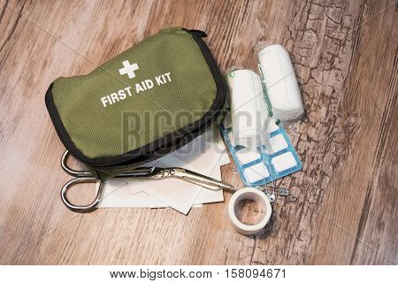 Green first aid kit on wooden background. Bandages, scissors and medicines