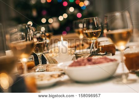 Dining table full of a variety of delicious festive food and wine with a Christmas tree in the background