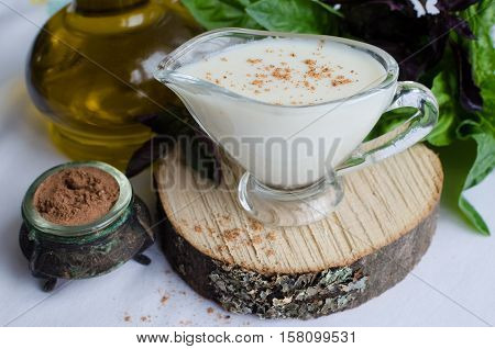 Classic European white sauce Bechamel in saucer with nutmeg basil and olive oil on white background. Bechamel sauce for traditional European dishes. Italian food concept. Selective focus.