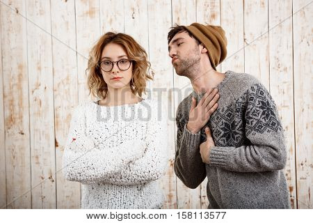 Young handsome man unnerve his girlfriend with crossed arms over wooden background. Copy space.