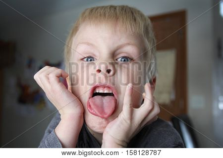 A six year old boy child is being funny and making a bratty face while sticking out his tongue.