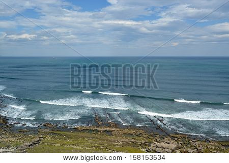 Green stone beach with sea waves. Sunny day with clouds. Photo from Portugal Atlantic seashore.