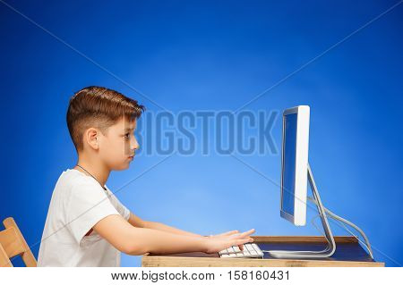 School-age boy sitting in front of the monitor laptop at blue studio backgroubd
